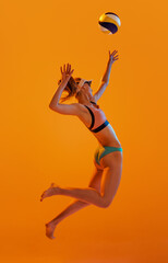 Fototapeta na wymiar Beach volleyball. Sportive young woman, volleyball player training with ball isolated on orange color background. Sport, healthy lifestyle, team, summer, fitness concept