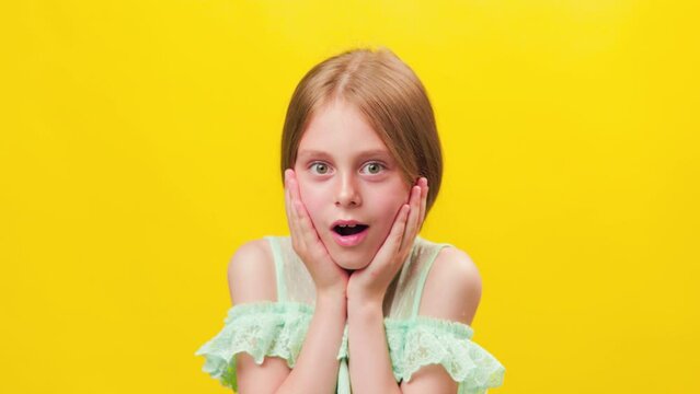 Surprised or scared little american kid girl with her hands on her face and her mouth open. child looking at camera and wondering, studio shot on yellow background