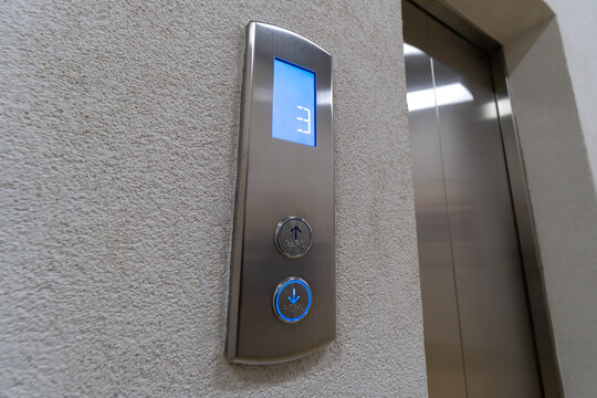 Close-up of the elevator call buttons up and down with Braille. Arrow of the elevator shows down the movement of the elevator to the third floor