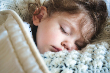 Close-up of a little girl sleeping peacefully wrapped up in a warm blanket