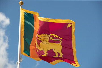 The flag of Sri Lanka flutters against a clear blue sky with white clouds. Close-up, perfect for news.