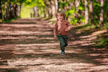 Fototapeta premium Happy little boy run on an alley in the park at summer