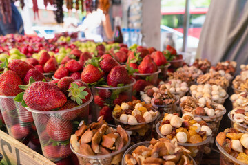 Close-up of strawberries, nuts, dried fruits, cherries, medlar in plastic cups. Counter with fruits, berries and dried fruits, a tourist place.