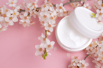 Obraz na płótnie Canvas Container with bodycare and skincare cream on a pink background with blooming cherry. Cosmetic facial skin care and spa. Natural treatment concept.