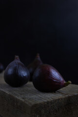 Three fresh figs on the rustic style wooden table. Black background. Low key.