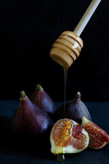 Three and a half fresh figs on the black background with honey dripping from wooden honey spoon