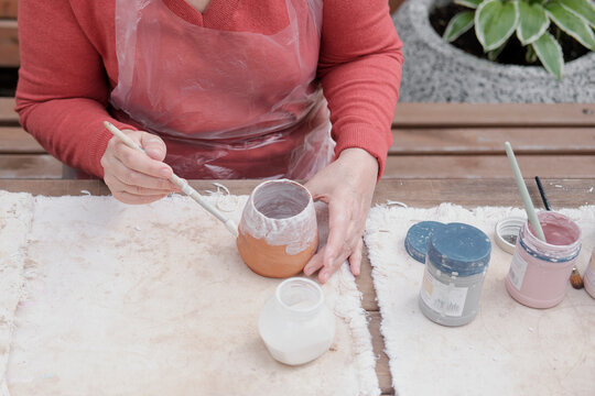 Hands Of Older Woman Painting Handmade Clay Vase With White Paint With Brush.