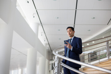 Businessman walking down spiral staircase in office with smartphone