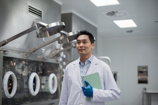 Male scientist walking through pharmaceutical manufacturing laboratory carrying a digital tablet