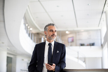 Middle Eastern businessman holding a smartphone in modern corporate office atrium