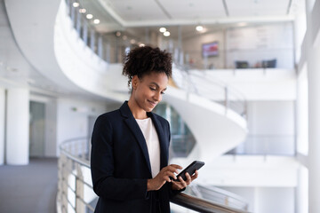 African American businesswoman using a smartphone in modern corporate office atrium