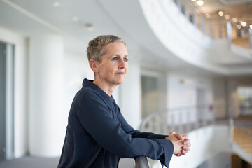 Senior businesswoman in a modern corporate office atrium looking out of window