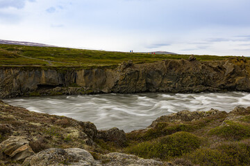 Force of the water running in Icelandic river flowing after Godafoss falls between volcanic rocks