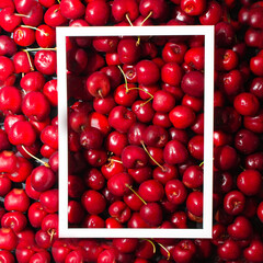 Red cherries background with white frame on it. Summer aesthetic concept. 