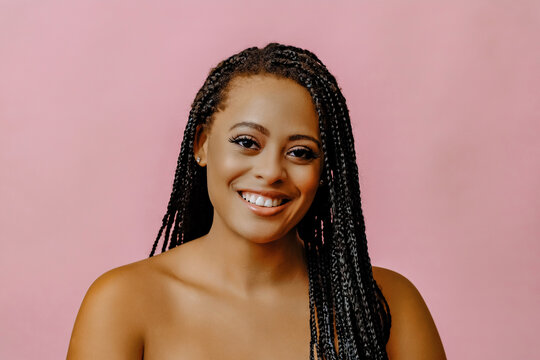 beauty headshot of smiling young adult black woman braid hair on pink background looking at camera studio shot