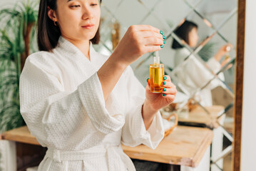 Facial Skincare. Happy Korean asian woman applying Facial serum using dropper standing in modern bathroom.