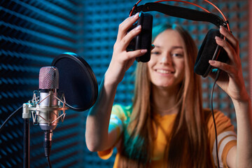 Girl in recording studio in headphones with mic over absorber panel background