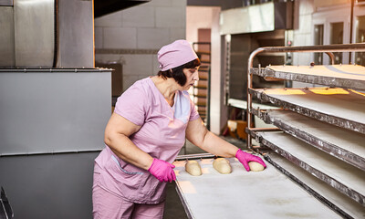 The baker forms the dough for baking bread and put it into oven-tray at the manufacturing