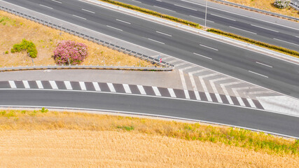 Motorway interchange in Italy. Each carriageway with three lanes of travel. On the sides of the road there are fields of wheat. There are no cars on the asphalt. - obrazy, fototapety, plakaty