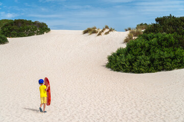 Fototapeta na wymiar Boy is climbing up the sand dune for sandboarding, Kangaroo Island, South Australia