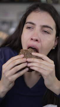 Woman eating tasty burger portrait face. Person takes a bite of hamburguer food. Vertical video