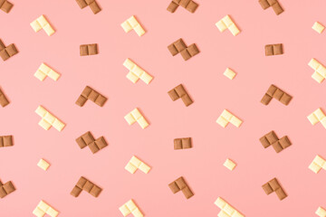 Pattern made with pieces of black and white chocolate bars on a pastel pink background. Minimal food aesthetic. Creative puzzle concept.