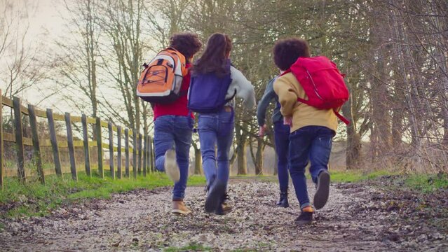 Children with school backpacks outdoors running away from camera along country lane - shot in slow motion