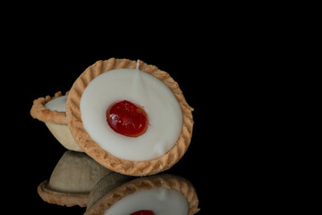Iced cherry bakewell tart on black background