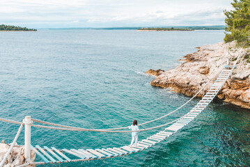 woman crossing suspension bridge sea on background