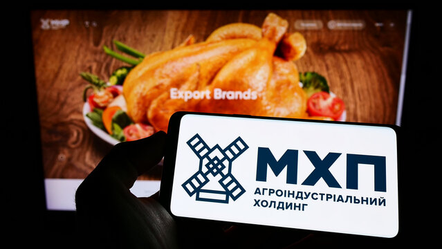 Stuttgart, Germany - 06-18-2022: Person holding cellphone with logo of Ukrainian company Myronivsky Hliboproduct (MHP) on screen in front of webpage. Focus on phone display.