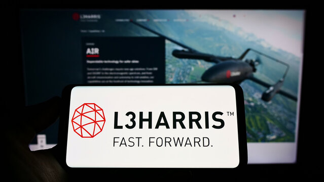 Stuttgart, Germany - 06-18-2022: Person holding smartphone with logo of US aerospace company L3Harris Technologies Inc. on screen in front of website. Focus on phone display.