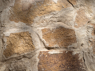 The old rough weathered brownish gray texture of the masonry of the stone wall. The background of the wall is made of stone material