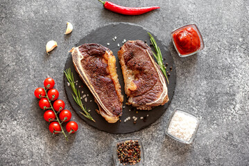 Grilled New York beef steak on the bone, herbs and spices on a stone background