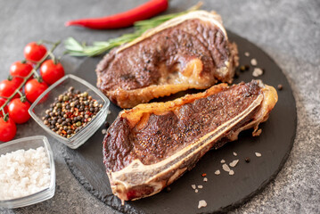 Grilled New York beef steak on the bone, herbs and spices on a stone background