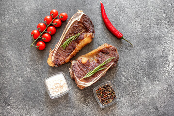Grilled New York beef steak on the bone, herbs and spices on a stone background