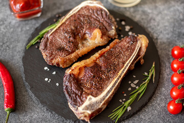 Grilled New York beef steak on the bone, herbs and spices on a stone background