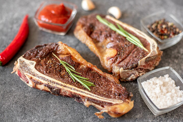 Grilled New York beef steak on the bone, herbs and spices on a stone background
