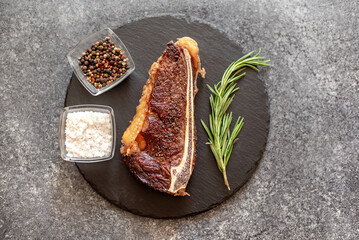 Grilled New York beef steak on the bone, herbs and spices on a stone background