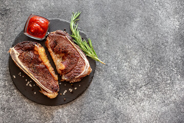 Grilled New York beef steak on the bone, herbs and spices on a stone background with copy space for your text