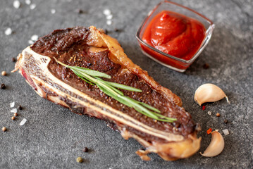 Grilled New York beef steak on the bone, herbs and spices on a stone background