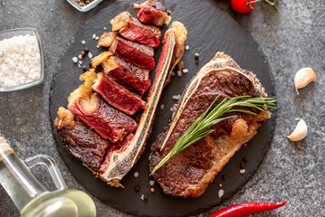 Grilled New York beef steak on the bone, herbs and spices on a stone background