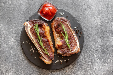 Grilled New York beef steak on the bone, herbs and spices on a stone background