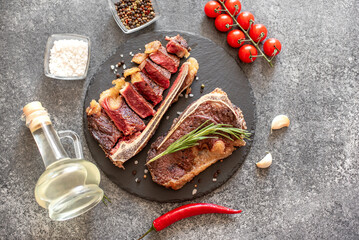 Grilled New York beef steak on the bone, herbs and spices on a stone background