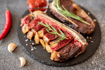 Grilled New York beef steak on the bone, herbs and spices on a stone background