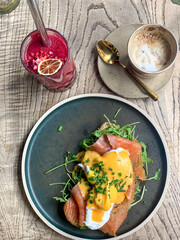 Healthy breakfast or brunch in cafe Eggs benedict with salmon and rocket on a toast with latte or cappuccino coffee and red berry smoothie. directly above