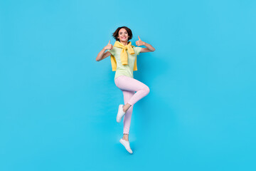 Fototapeta na wymiar Full body photo of cute young brunette lady jump show thumb up wear t-shirt trousers footwear isolated on blue background