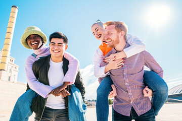 outdoors photo of happy boyfriends piggybacking their girlfriends. Group Of Friends Having Fun Together. Cheerful young loving couples friends walking in a park.