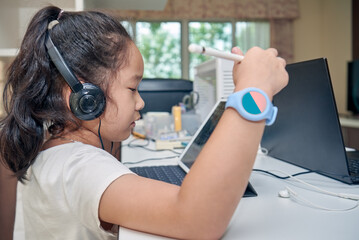 Little preschool girl with headphones using digital tablet computer for online education at home office.