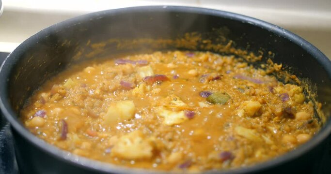 Close up shot of Indian dal (lentil) been cooked in a black pan with cauliflower, chickpeas, onions and red lentils over an induction cooktop in the kitchen