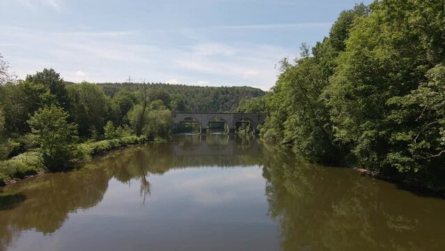 Old brick train trestle leading over the Sieg river near Schladern, Germany on a sunny spring day. Low flying aerial approach